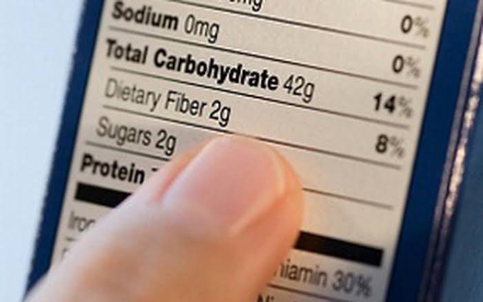 Person reading food labels at supermarket examining nutrition panel and ingredients list for sugars, fibre, emulsifiers, and artificial additives for liver and digestive health