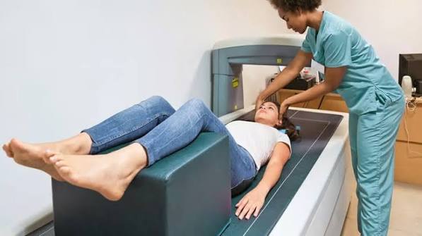 Bone density test patient lying on DEXA scanner table while radiographer operates the machine and the arm passes over the hip area measuring bone mineral density with T-score results visible on screen