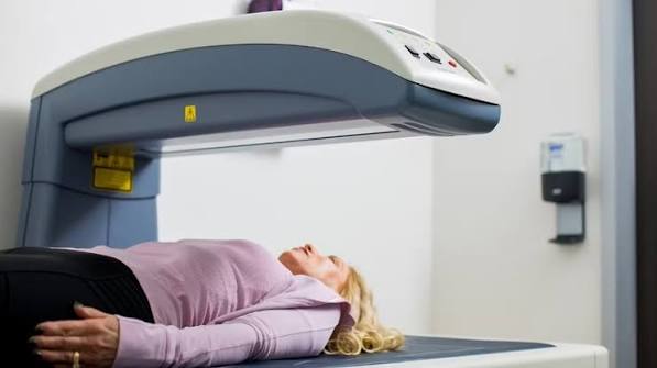 DEXA scan machine in a clinical radiology department showing the large open gantry with a flat padded examination table and movable scanner arm used for bone density measurement at the hip and lumbar spine