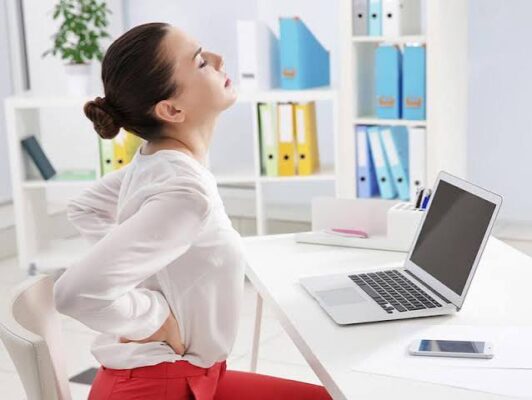 Office worker standing up from desk to take a movement break and prevent sitting too long and digestive symptoms including constipation and bloating